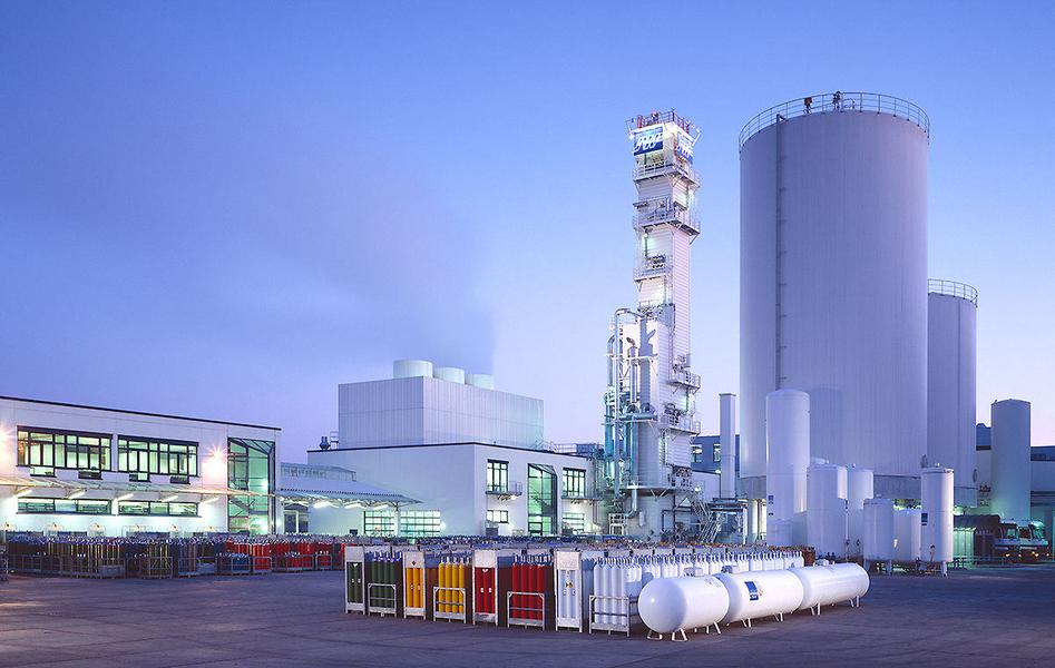Werksansicht Ein Industriekomplex mit mehreren großen Behältern, Maschinen und Lagerräumen. Im Vordergrund stehen farbige Gaskontingente. Der Himmel ist hellblau, was auf Morgen- oder Abendlicht hinweist. Die Struktur zeigt einen modernen, funktionalen Baustil.