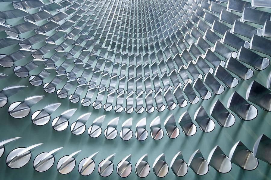 Schaufeltraeger Eine abstrakte Struktur mit sich spiralförmig anordnenden, glänzenden Metallteilen. Die Elemente sind halbrund und reflektieren das Licht, was einen dynamischen Eindruck erzeugt. Der Blickwinkel ist von unten nach oben gerichtet, wodurch die Tiefe der Form betont wird.