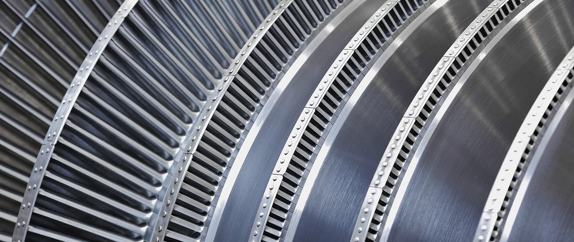 Dampfturbine Detailaufnahme von mehreren Schaufelreihen einer Turbine. Die metallischen Oberflächen sind glatt und reflektieren das Licht, während die Schaufeln eine präzise und gleichmäßige Anordnung zeigen.