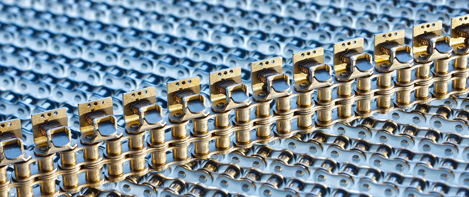 Antriebstechnik Ketten Detailaufnahme von metallischen Bauteilen, die in einer geraden Linie angeordnet sind. Die Teile haben eine goldene Farbe und sind auf einer blauen, strukturierten Fläche platziert.